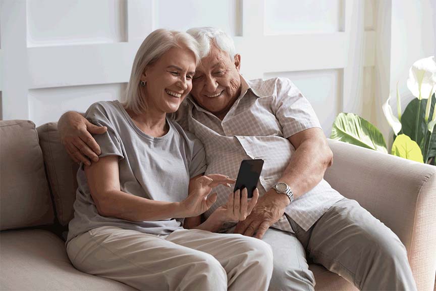 An older couple smiling while holding a phone.