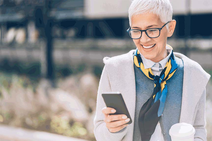 An older woman smiling at her phone.